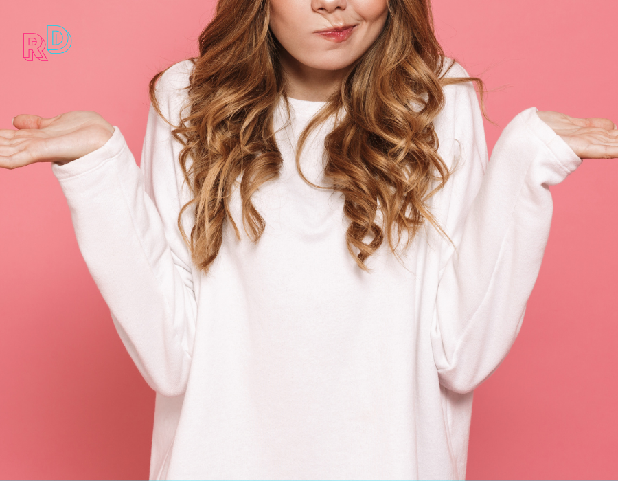 Woman in white sweater shrugging against pink background
