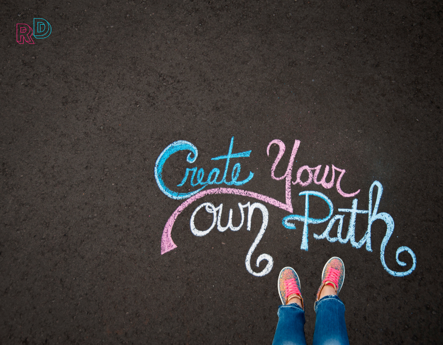 Chalk on pavement that says create your own path with colourful sneakers