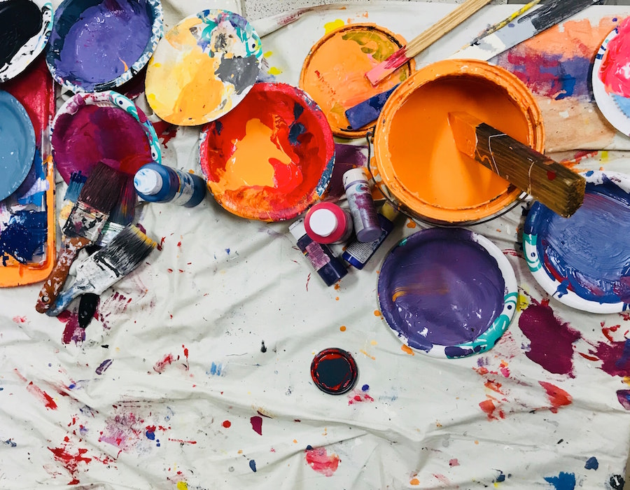Open paint cans in a variety of colours on a white drop sheet